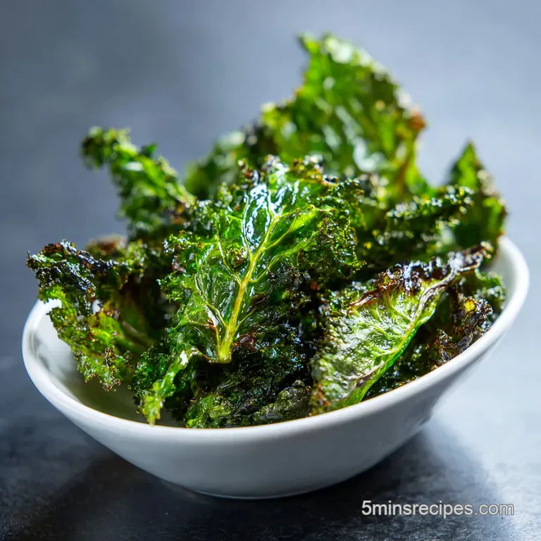 Pile of dark green kale chips artfully arranged on a white plate, showcasing their crispy, slightly jagged edges and invit...