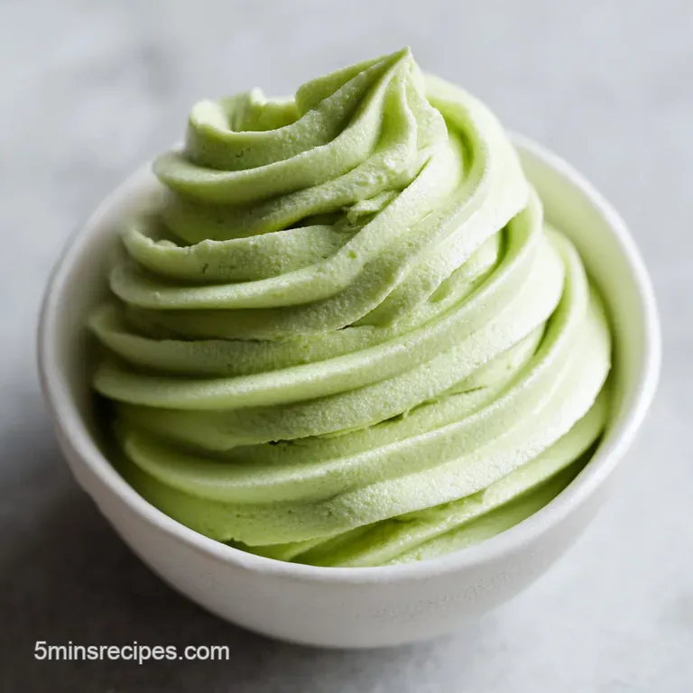 Elegant swirls of pale green frosting piped onto a white ceramic plate, accented by crushed emerald nuts.