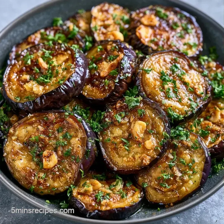 Slices of caramelized eggplant arranged on a white ceramic plate, drizzled with glistening oil and fresh green herbs.