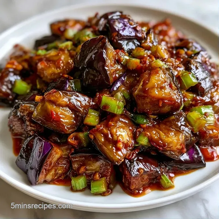 A vibrant medley of saut&eacute;ed purple eggplant and olives served on a white platter with a drizzle of golden olive oil.